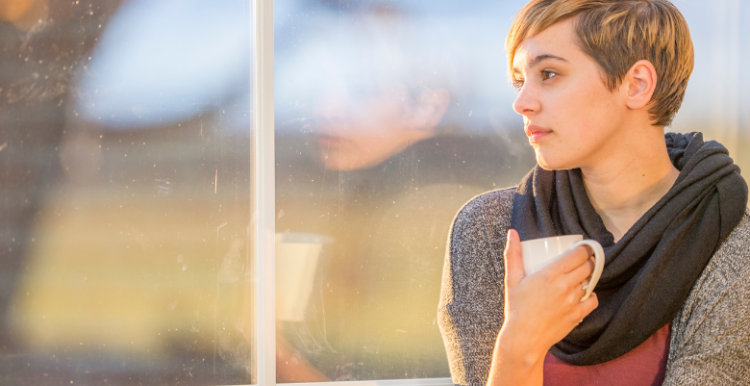 An image of a person holding a cup gazing out of a window