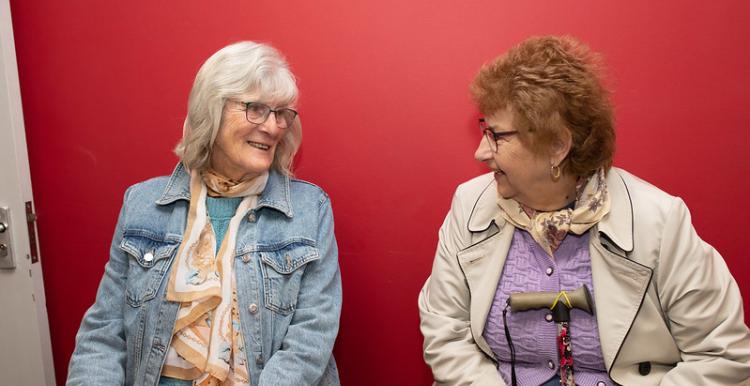 Two women sat down talking to each other, waiting for the bus