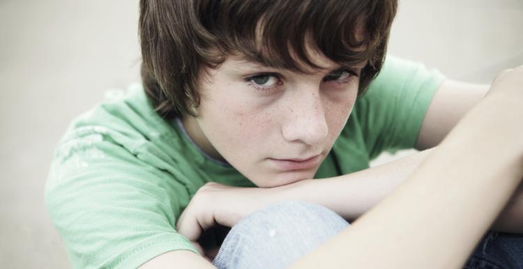 A young boy sitting down hugging his knees