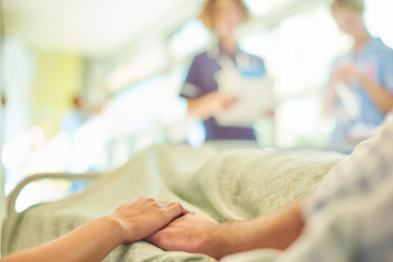 Patient on hospital bed holding hands with a relative